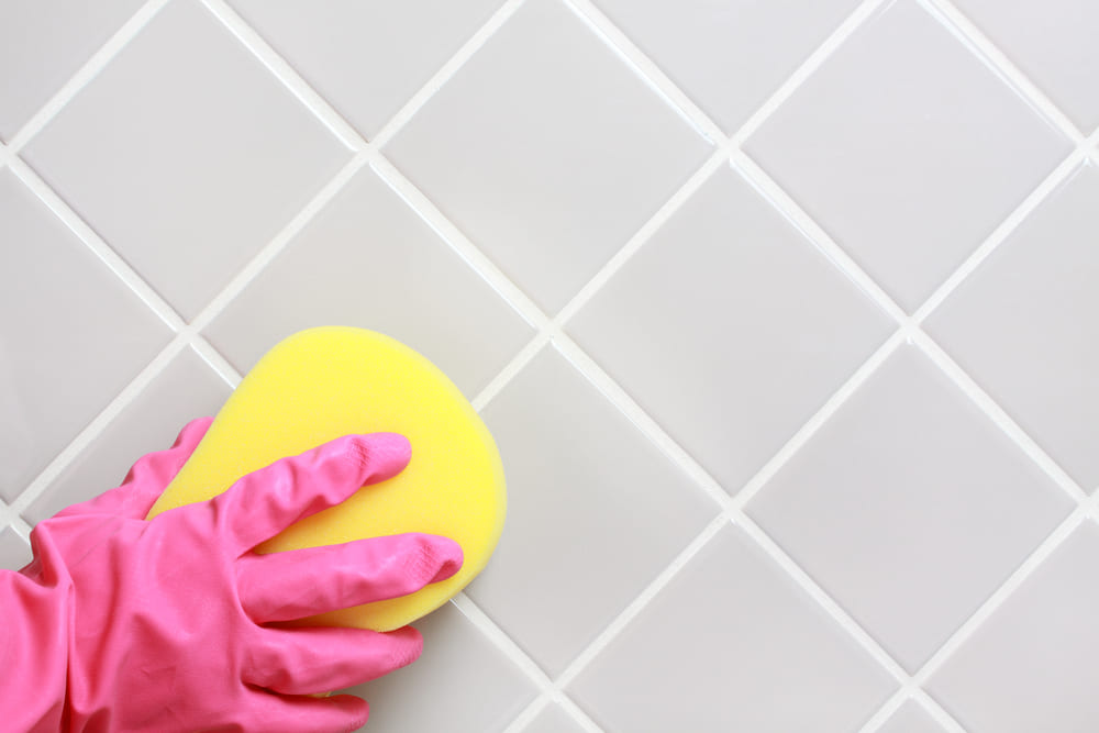 Someone cleaning the grout between tiles with sponge