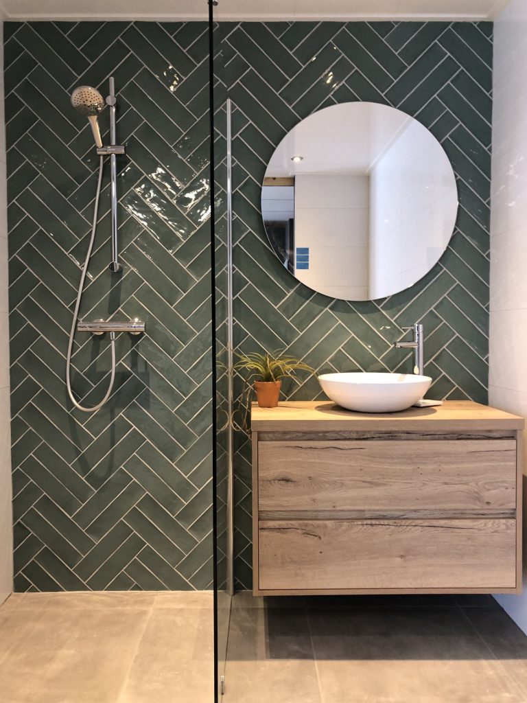 green bathroom with green herringbone tiles and wooden bathroom furniture